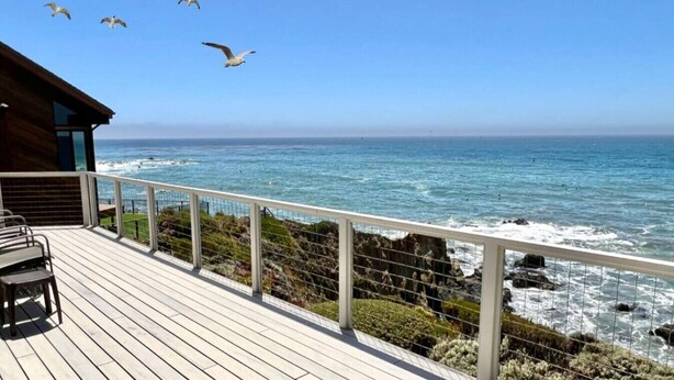 A wooden deck with a railing overlooking the ocean, with seagulls flying above.