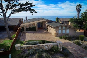 A coastal property with a stone driveway, a covered patio, and a view of the ocean.