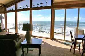 A room with large windows overlooking the ocean, a lamp on a table, and a view of the beach.