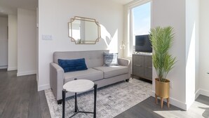 Un salon moderne avec un canapé gris, une table basse ronde, un grand miroir, un téléviseur et une plante en pot.