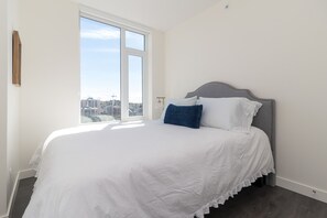 Une chambre avec une grande fenêtre, un lit avec une literie blanche et une vue sur le paysage urbain.