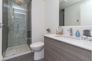 Une salle de bain moderne avec une douche à parois de verre, des toilettes blanches, un meuble-lavabo avec un miroir et un évier.