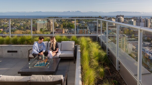 Une terrasse sur le toit dotée d’une balustrade en verre, d’un espace salon extérieur et offrant une vue sur le paysage urbain et les montagnes.