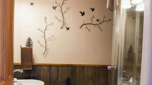A bathroom with a wooden wall, a white sink, a toilet, and a glass shower enclosure.