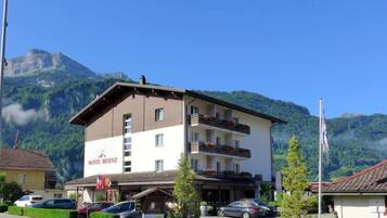 Un hôtel appelé HOTEL BRIENZ, avec une structure à deux étages, des balcons ornés de jardinières et un paysage montagneux en toile de fond.