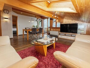 A modern living room with a glass coffee table, leather sofas, a flat-screen TV, and a dining area with a wooden table and chairs.