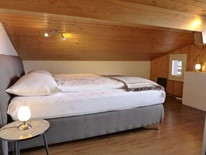 A cozy bedroom with a wooden ceiling, a bed with white bedding, a bedside lamp, and a small round table.