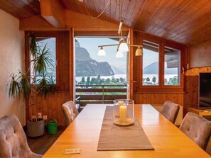 A wooden interior with a long table, chairs, a TV, and a view of mountains and water.
