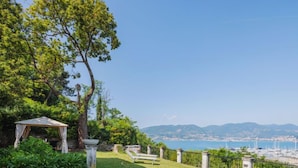Un jardin agrémenté d’un belvédère, d’un banc et offrant une vue sur la mer et les montagnes.