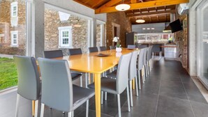 Un comedor amplio con una larga mesa de madera y sillas modernas, ventanas grandes y un fondo de pared de piedra.