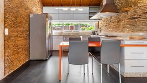Una cocina moderna con pared de piedra, vigas de madera en el techo y vista a zonas verdes.