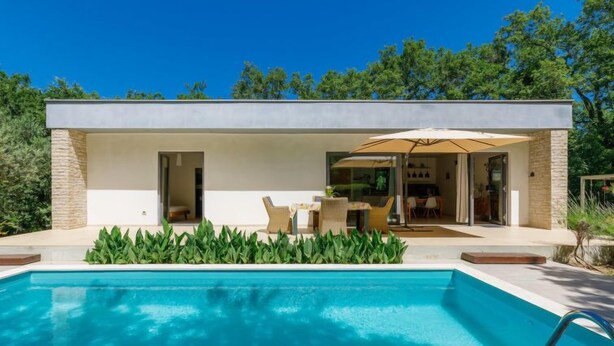 Une maison moderne dotée d’une piscine, d’un espace salon extérieur et d’une porte vitrée donnant sur un patio.