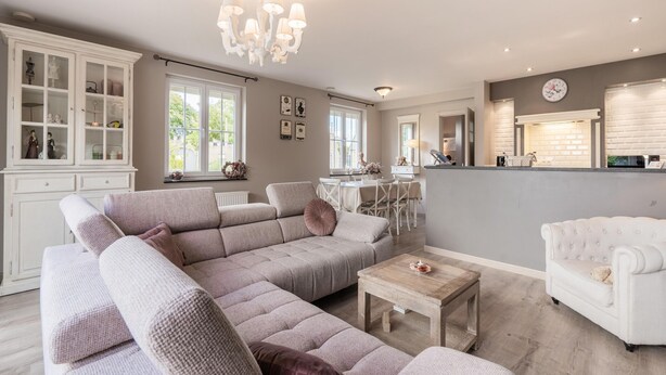 A spacious living room with a large sectional sofa, a white armchair, and a wooden coffee table. A dining area with a white table and chairs is visible in the background. - Inviting holiday home in Nieuwpoort with garden (Nieuwpoort)