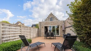 A patio area with two lounge chairs and a table, a wooden fence, and a brick building with a window and a chimney. - Inviting holiday home in Nieuwpoort with garden (Nieuwpoort)