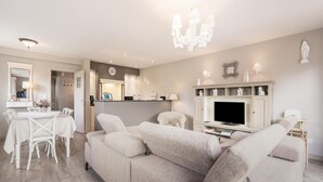 A modern living room with a beige sofa, a dining table with chairs, a TV, and a chandelier. - Inviting holiday home in Nieuwpoort with garden (Nieuwpoort)