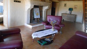 Uma sala de estar com lareira, poltronas de couro, uma mesa pequena com um vaso e teto de madeira.