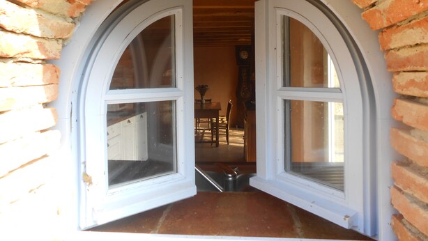 Uma porta com duas janelas emolduradas em branco que dão para um espaço interior com piso de madeira e uma área de refeições visível ao fundo.