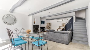 A modern living room with a grey sofa, a dining table with blue chairs, and a staircase.