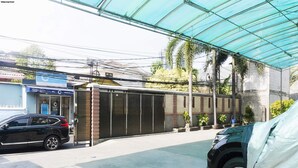 A covered parking area with a gated entrance, a black car parked inside, and a building with a blue sign in the background.