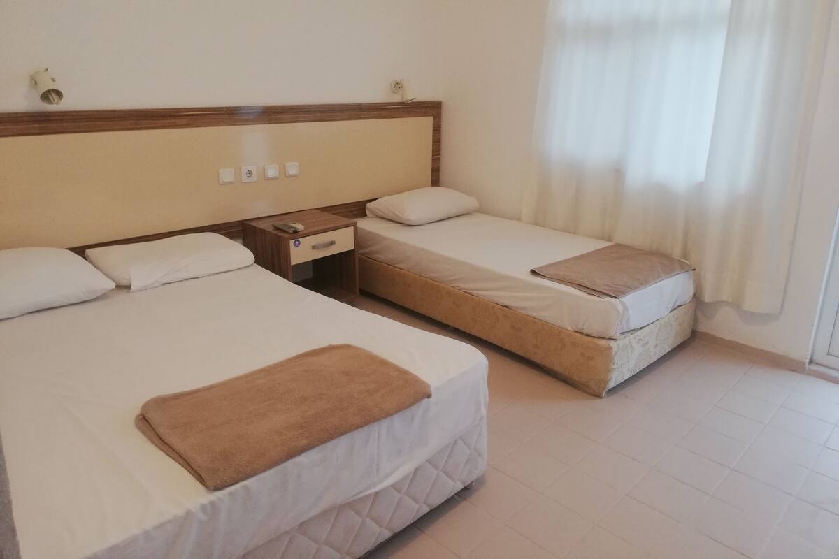 A hotel room with two beds, a wooden nightstand, and a window with curtains.