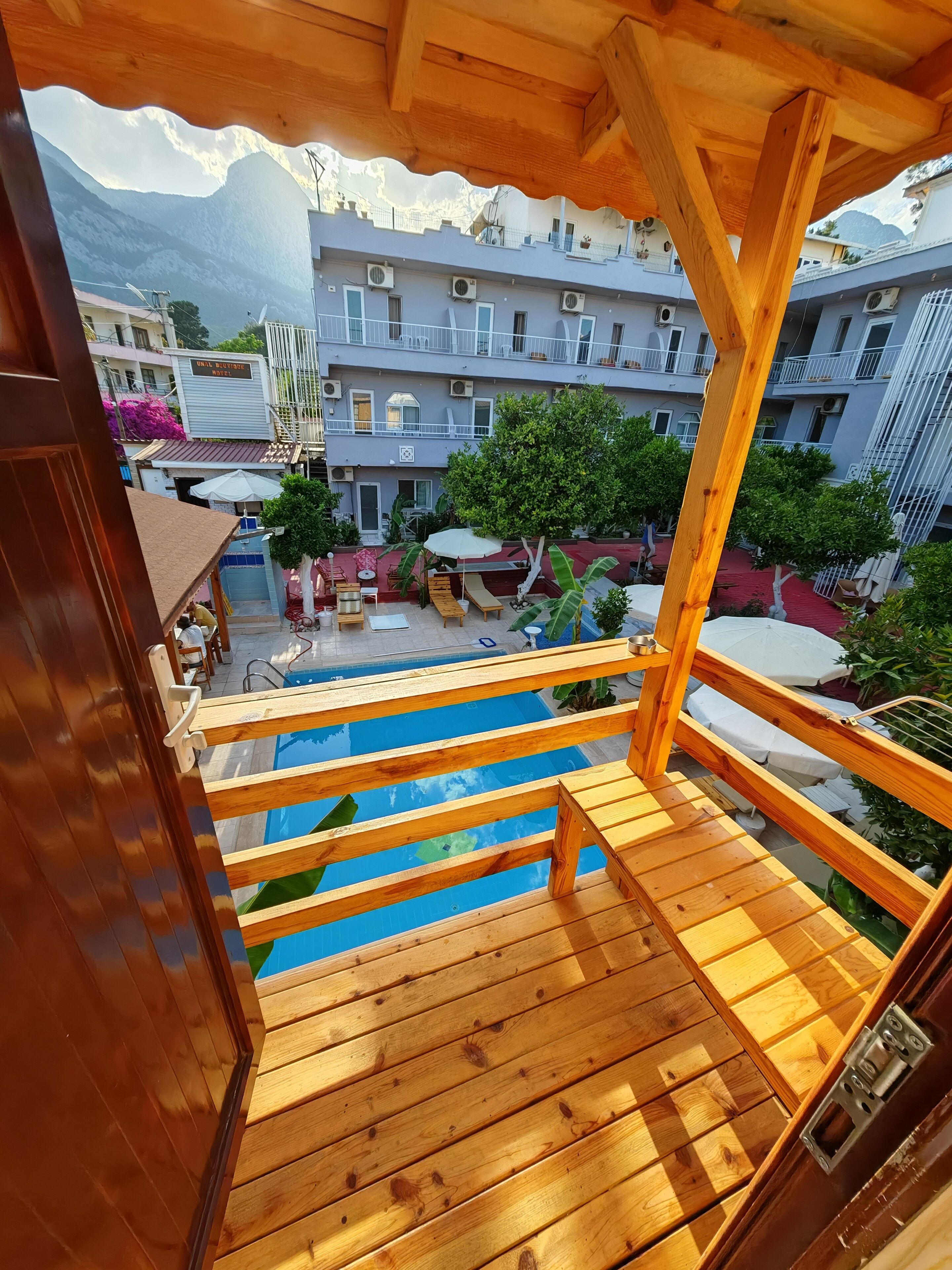 Une terrasse en bois avec une piscine, donnant sur une cour intérieure bordée de bâtiments et avec une montagne en toile de fond.