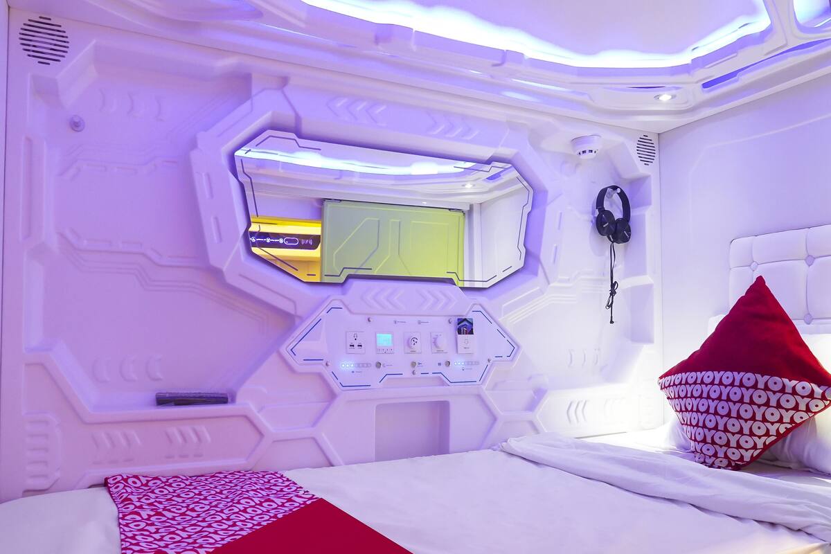 A modern, high-tech room with a control panel, a bed with a red and white patterned bedspread, and a red pillow.