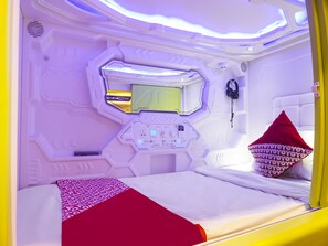 A room with a bed, a control panel, a mirror, and a pillow with a repeating pattern. - Hotel O Fiducia Capsule Hotel (Jakarta)