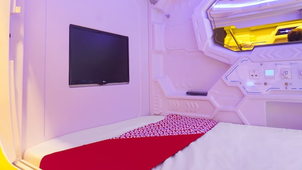 A futuristic room with a bed, a flat-screen TV, and a control panel. - Hotel O Fiducia Capsule Hotel (Jakarta)