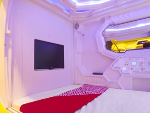 Une pièce futuriste équipée d’un lit, d’un téléviseur à écran plat et d’un panneau de commande.