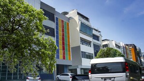 A modern building with a colorful facade, parked cars, and a clear sky. - Hotel O Fiducia Capsule Hotel (Jakarta)