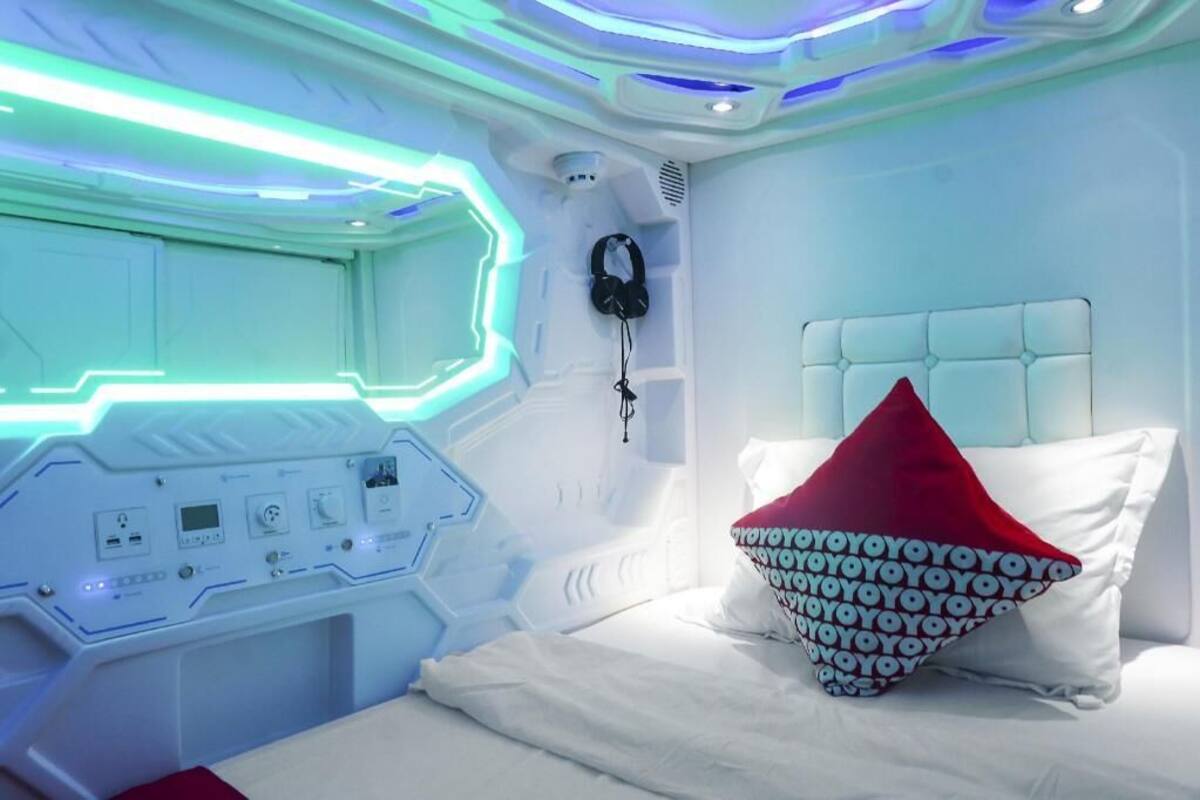 A modern room with a control panel, a bed with a red pillow, and a headset on the wall.
