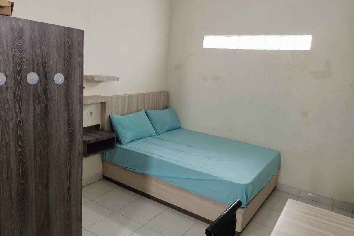 A small, simple room with a bed, a wooden wardrobe, and a window.