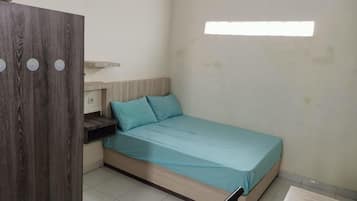 A small, simple room with a bed, a wooden wardrobe, and a window.