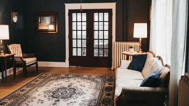 A room with a dark patterned wall, a large window with a view, a white sofa, a wooden floor, and a patterned rug. - Voted the Top short-term rental in BISMARCK!! (Bismarck)