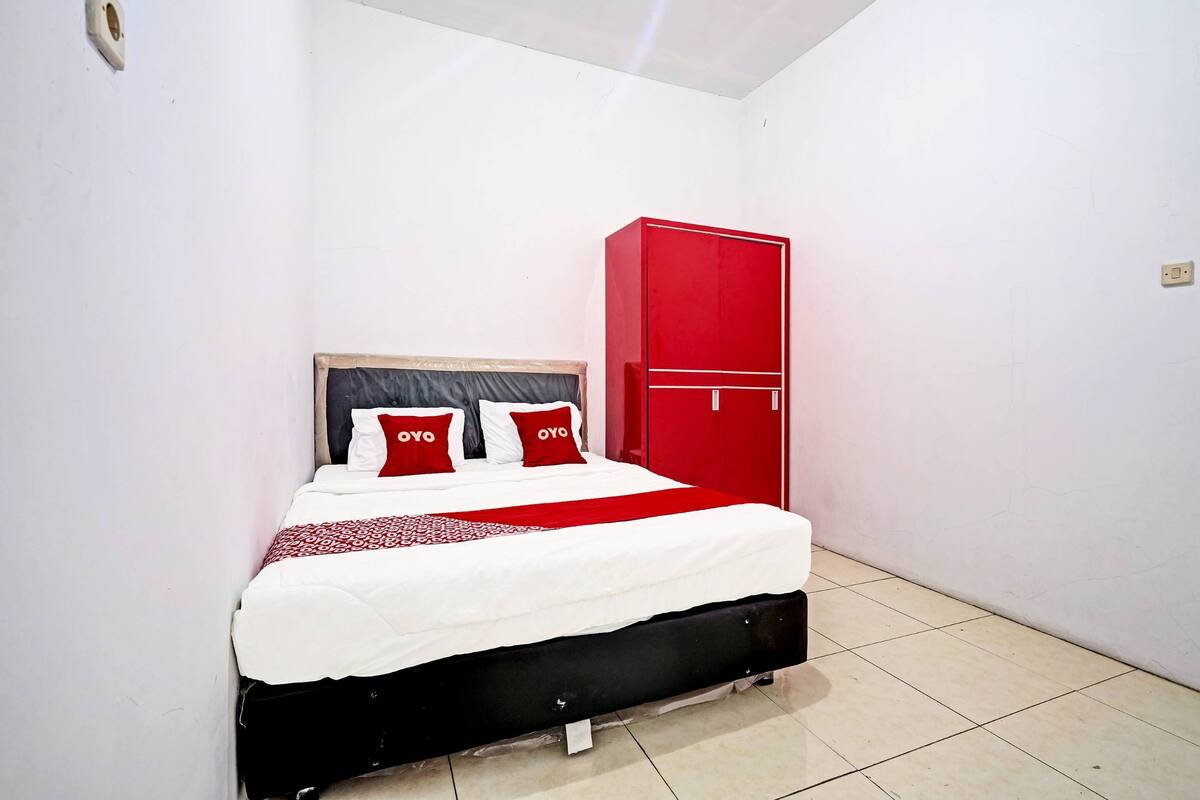 Un lit avec un cadre noir, du linge de lit blanc et des oreillers rouges.