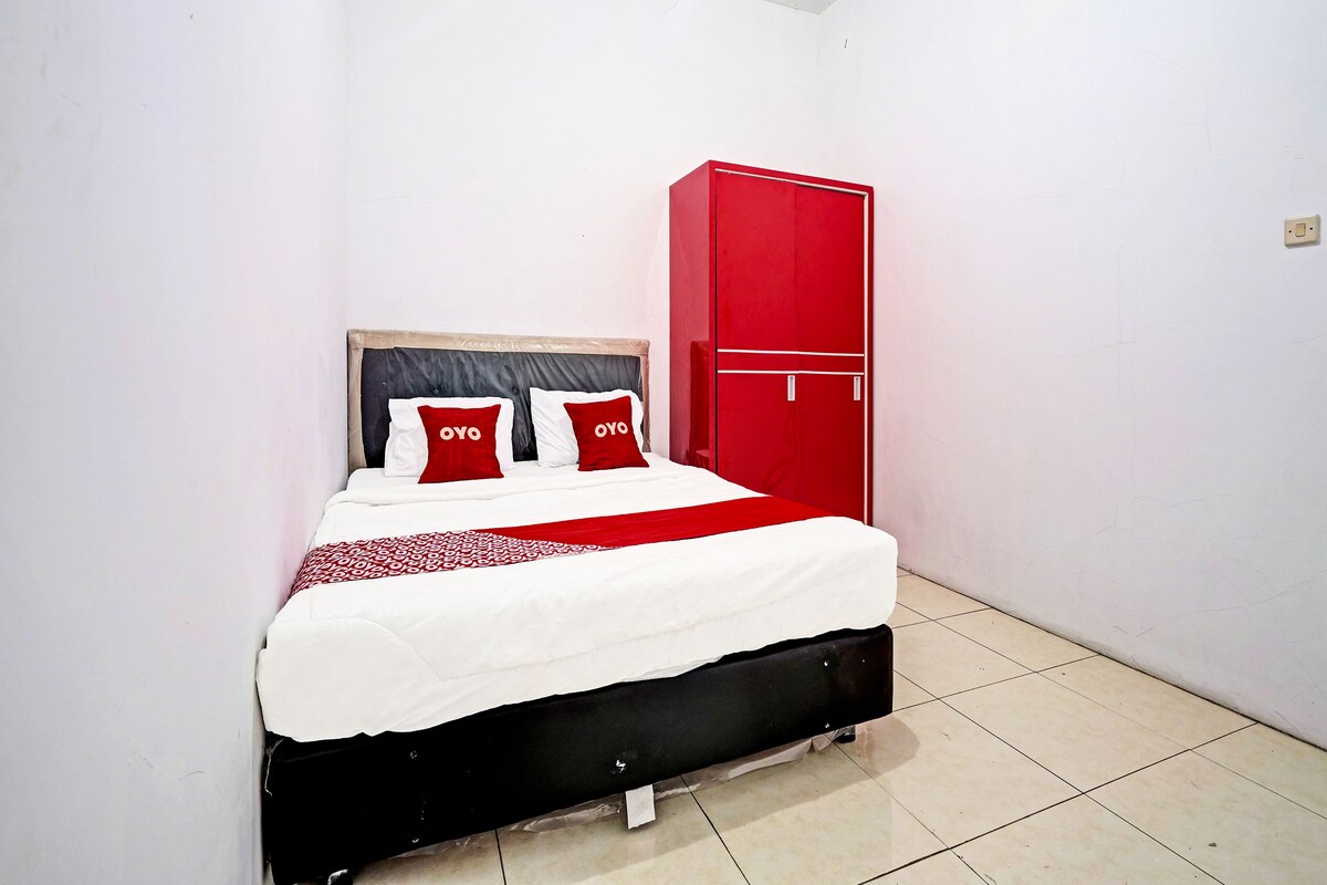 Een bed met een wit-rode dekbedovertrek, twee rode kussens met de tekst “OYO” erop, en een rode garderobe tegen een witte muur.