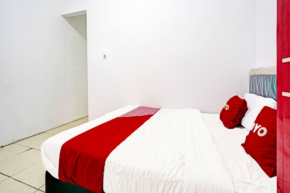 A bed with a red and white bedspread, two red pillows, and a white headboard.