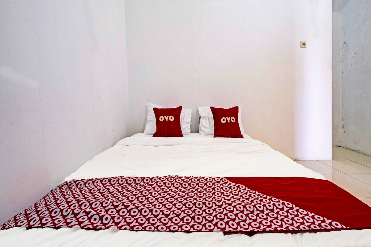Un lit avec une literie blanche et deux oreillers rouges sur lesquels est inscrit le mot « OYO ».