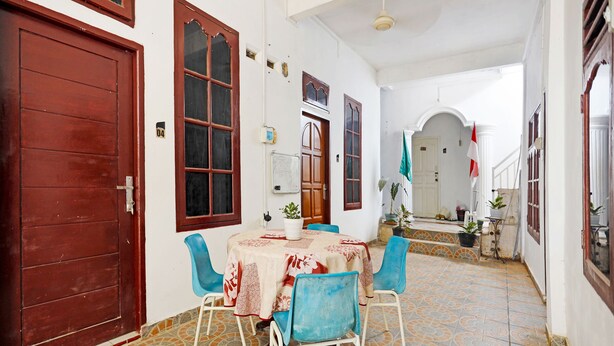 A dining area with a round table, blue chairs, and a patterned tablecloth. There are potted plants and a whiteboard on the wall. - OYO 91314 Zein House (Batam)