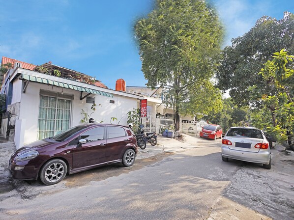 A residential street with houses, parked cars, and a tree. - OYO 91314 Zein House (Batam)