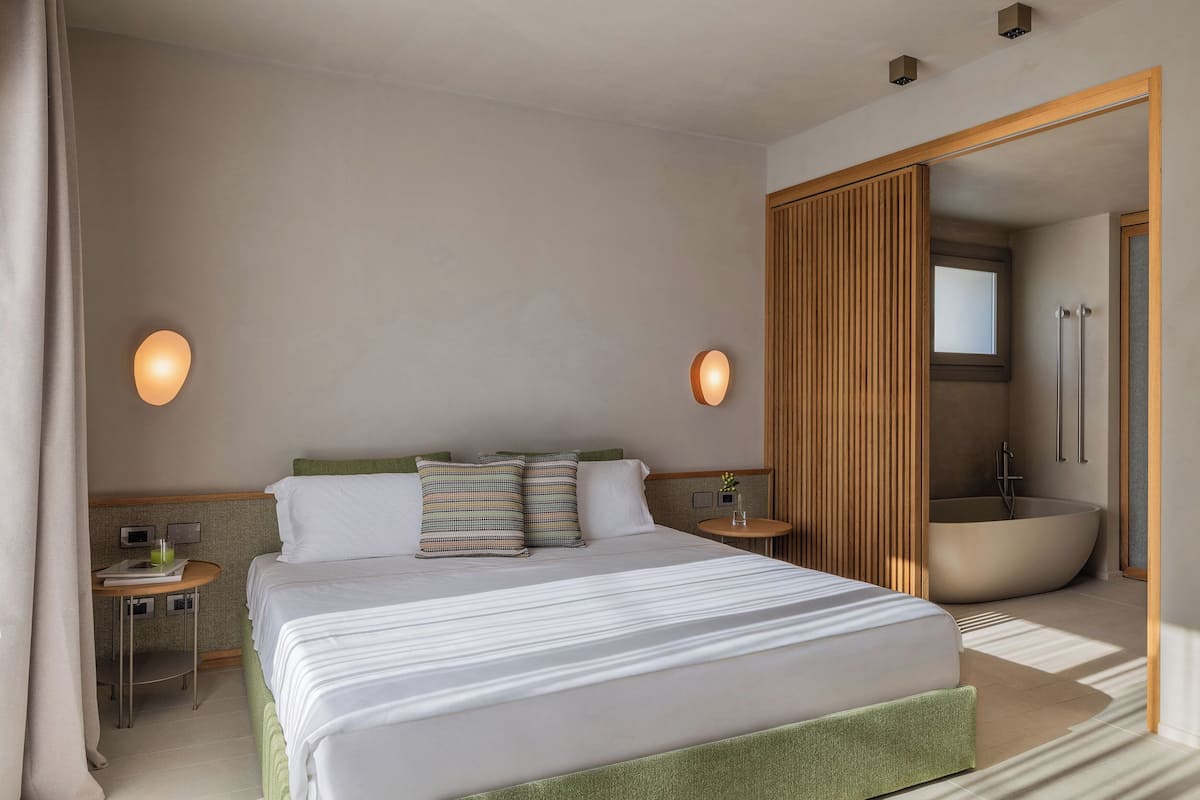 Ein modernes Hotelzimmer mit einem großen Bett, einer Holzkommode, einem runden Tisch mit einem Stuhl und einer integrierten Badewanne.