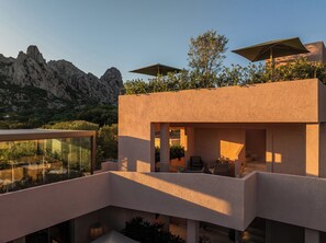A modern outdoor terrace with seating and a glass enclosure, overlooking a mountainous landscape. - La Suera San Pantaleo (Olbia)