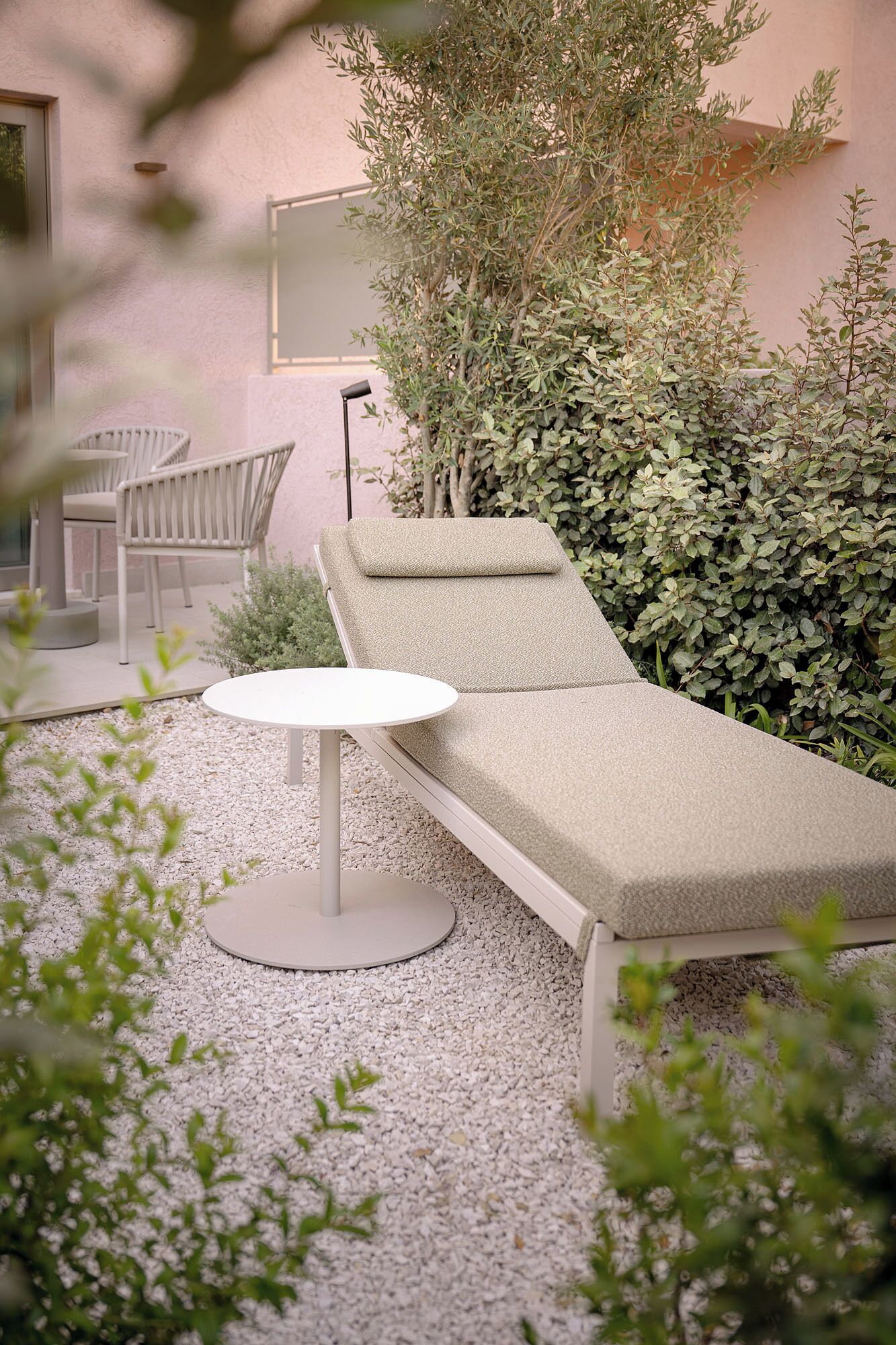 A lounge area with two cushioned chairs and a small round table, surrounded by gravel and greenery.