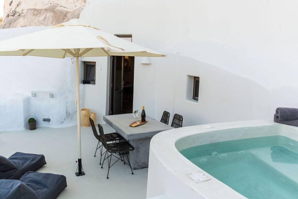 Un espacio exterior moderno con un jacuzzi, una mesa con sillas y un paraguas grande.