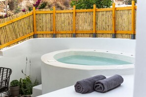 A hot tub in a corner with a bamboo fence, a chair, and towels. - Afora Houses (Santorini)