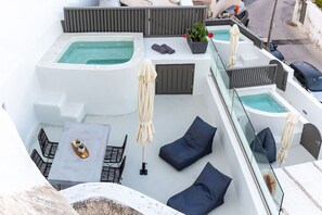 A rooftop terrace with two hot tubs, seating areas, and a table with chairs. - Afora Houses (Santorini)