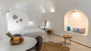 Habitación moderna y minimalista con cama, una mesa redonda con frutas y un pequeño rincón de descanso.