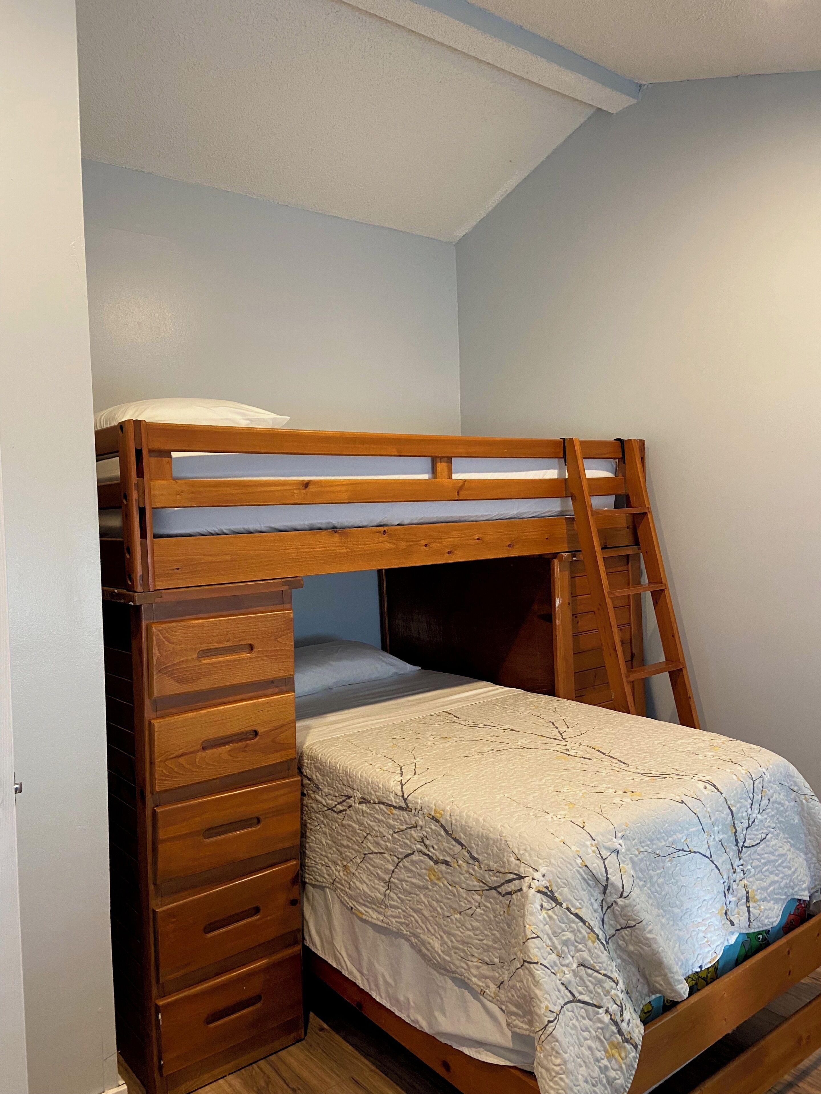 A bunk bed with a ladder, wooden drawers, and a patterned bedspread.
