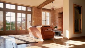A spacious living room with a leather sofa, large windows, and a stone wall.