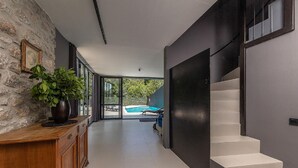 A modern hallway with a stone wall, a wooden console, and a staircase leading to a balcony with a pool.